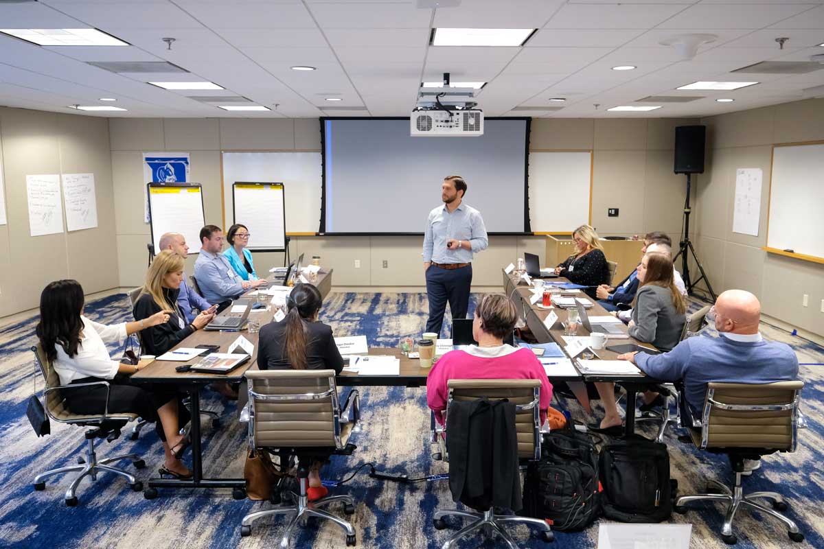 Participants seated at conference tables engage with faculty in strategic communication course 