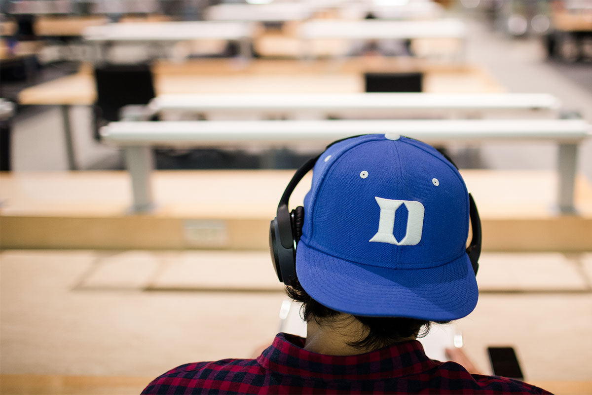 Photo of Student Wearing a Duke hat sitting in library